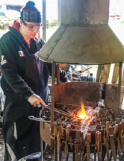 A young woman heating metal in a blacksmith's forge