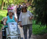 Batsford workshop participants on a path through the trees, with a mobility scooter user and their friend in the foreground