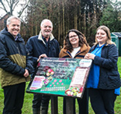 Photo of GRCC's Sabrina Dixon and Highnam Parish Councillors and Clerk next to a colourful information board in their Community Orchard